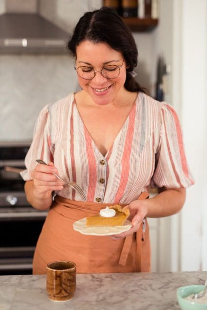 Joy the Baker holds a slice of sweet potato pie on a small plate.