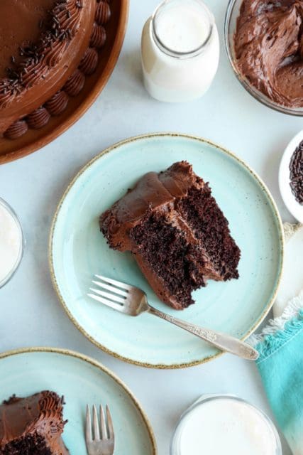 Slice of chocolate cake on a pale green plate with a fork and chocolate frosting.