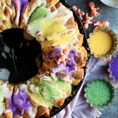 A New Orleans King Cake baked in a cast iron skillet with green, gold, and purple sprinkles