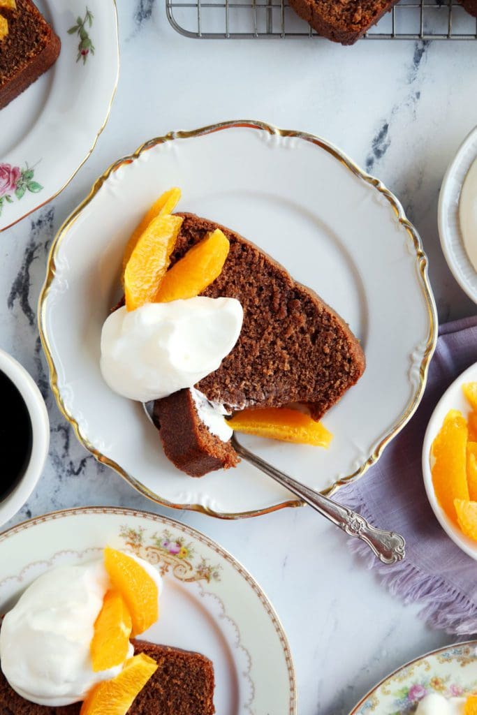 Fork into slice of loaf cake with whipped cream and oranges.