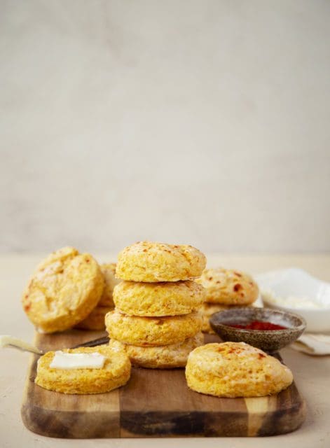 Sweet potato biscuit recipe stacked on a cutting board with butter.