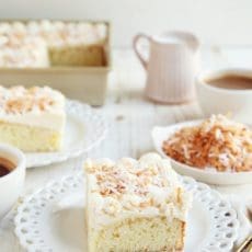 Slice of coconut cake on small white plate with coffee.