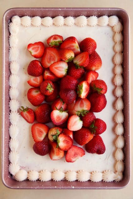 fresh strawberries atop frosted strawberry cake.