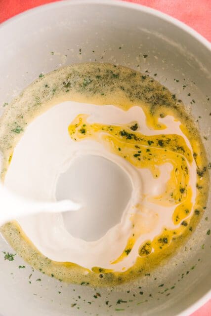pouring milk into a pot with herbs and butter for mashed potatoes