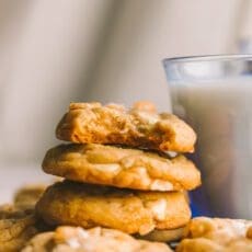 a stack of white chocolate macadamia nut cookies with a bite taken out of the top one with milk