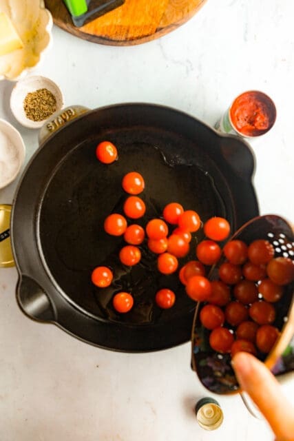 adding grape tomatoes to a cast iron pan to cook
